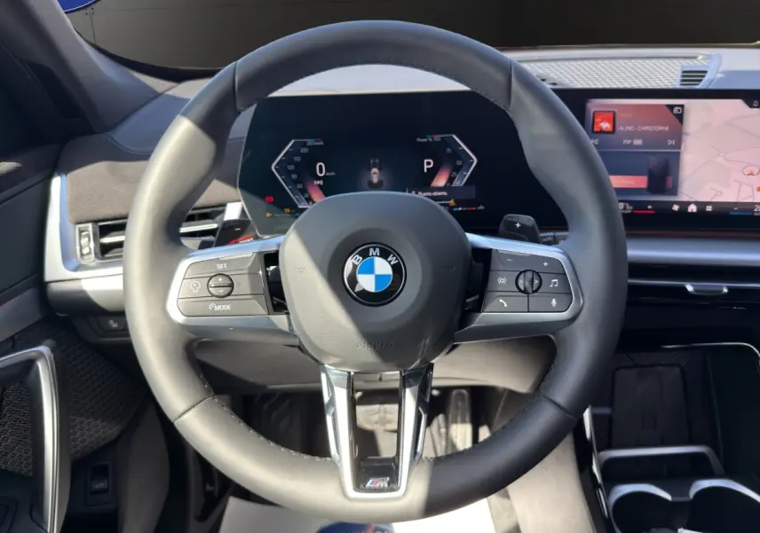 Vue rapprochée du volant en cuir noir multifonction du BMW X1 sDrive20d 2025 avec tableau de bord numérique et écran tactile.
