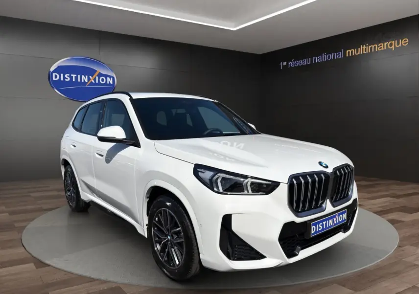 BMW X1 sDrive20d blanc vue 3/4 avant avec calandre noire et jantes foncées dans showroom