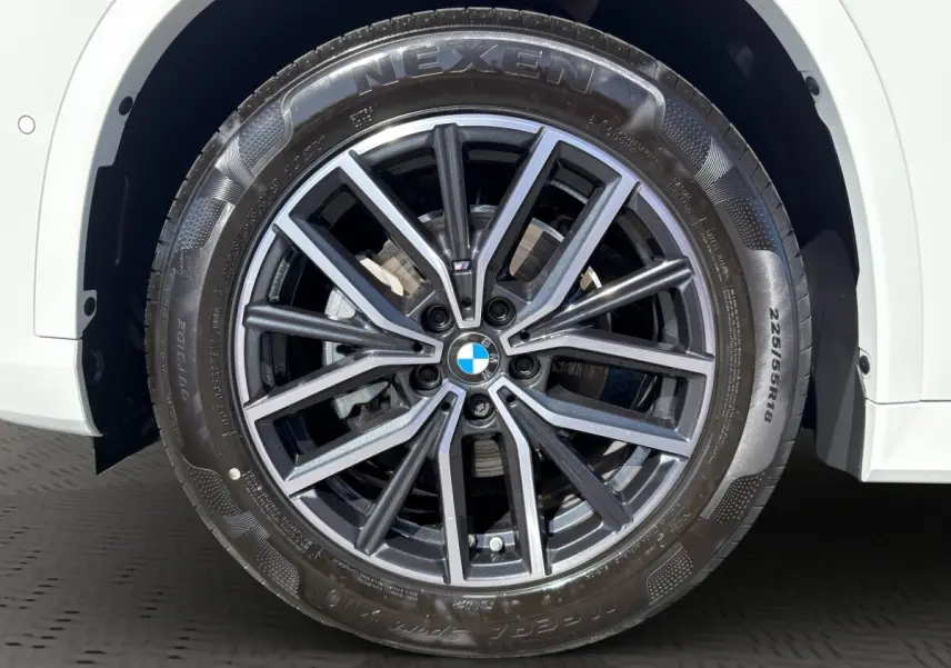 Gros plan sur la roue avant droite d'une BMW X1 blanche avec jante alliage M Sport et pneu Nexen.