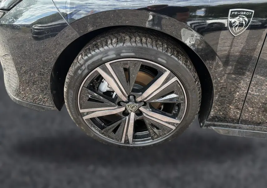 Gros plan sur la roue avant gauche noire d'une Peugeot 308 1.2 hybrid 145 GT avec jante alu au design moderne.
