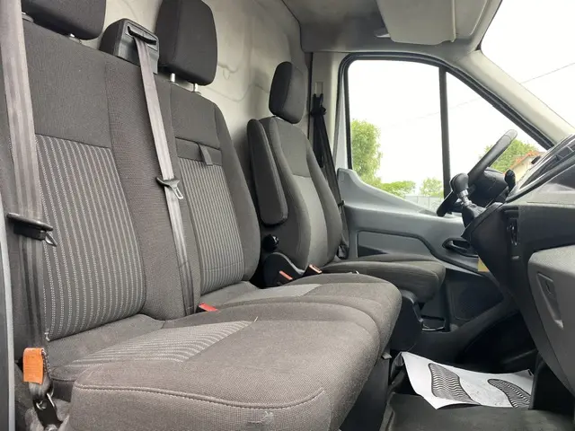 Vue intérieure côté conducteur du Ford Transit Fourgon 2019, sièges gris foncé avec accoudoir central et volant visible.