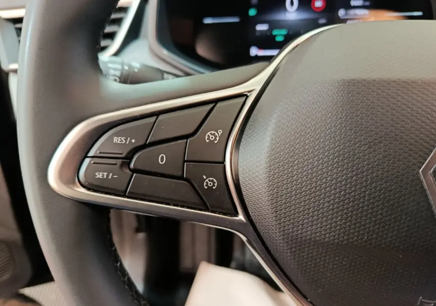 Gros plan sur le volant cuir synthétique de la Renault Clio 2025 avec commandes de régulateur de vitesse côté gauche.