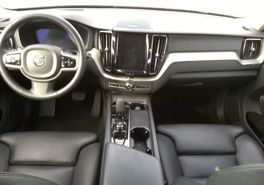 Vue intérieure avant du Volvo XC60 2023, tableau de bord et sièges en cuir noir avec console centrale moderne.