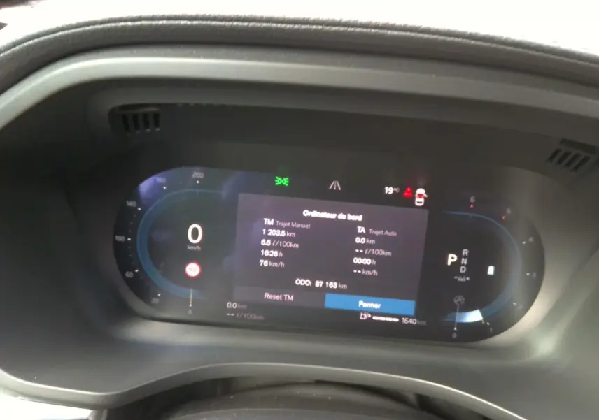 Gros plan sur l'ordinateur de bord numérique du Volvo XC60 bleu, affichant les données de trajet et la vitesse à 0 km/h.