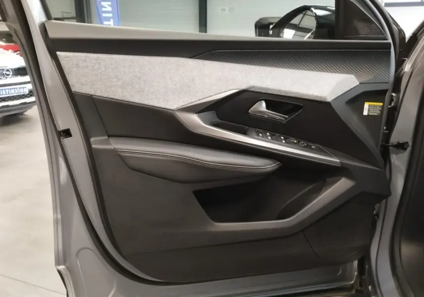 Vue intérieure de la porte avant gauche gris Artense du Peugeot 3008 2024 avec habillage tissu et commandes électriques.