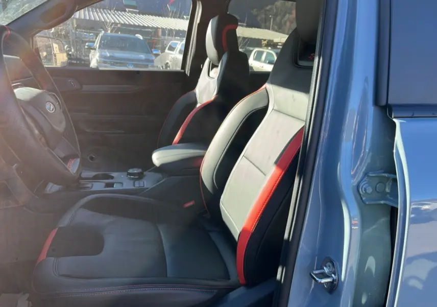 Vue intérieure côté conducteur du Ford Ranger Raptor gris commandeur, sièges sport cuir noir et rouge avec accoudoir central.