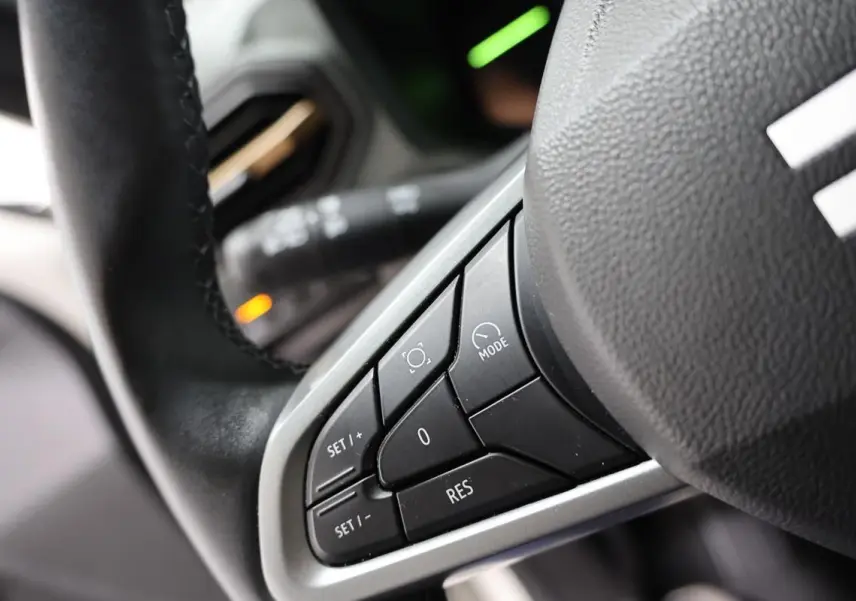 Gros plan sur les commandes au volant du Dacia Duster 2024, montrant les boutons de réglage et mode, intérieur noir.