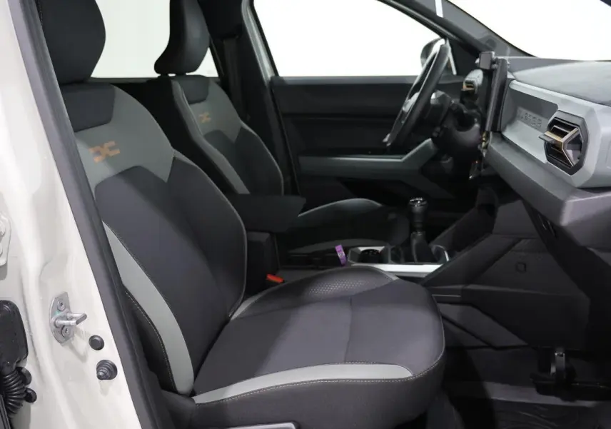 Vue intérieure côté conducteur du Dacia Duster 2024 avec sièges tissu bi-ton et tableau de bord moderne.