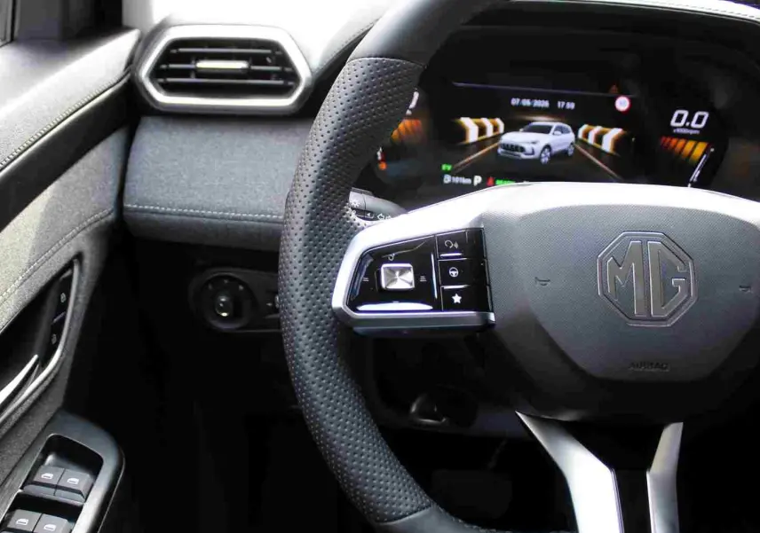 Vue intérieure centrée sur le volant perforé noir du MG ZS 1.5L Hybrid+ avec tableau de bord numérique affichant un véhicule blanc.