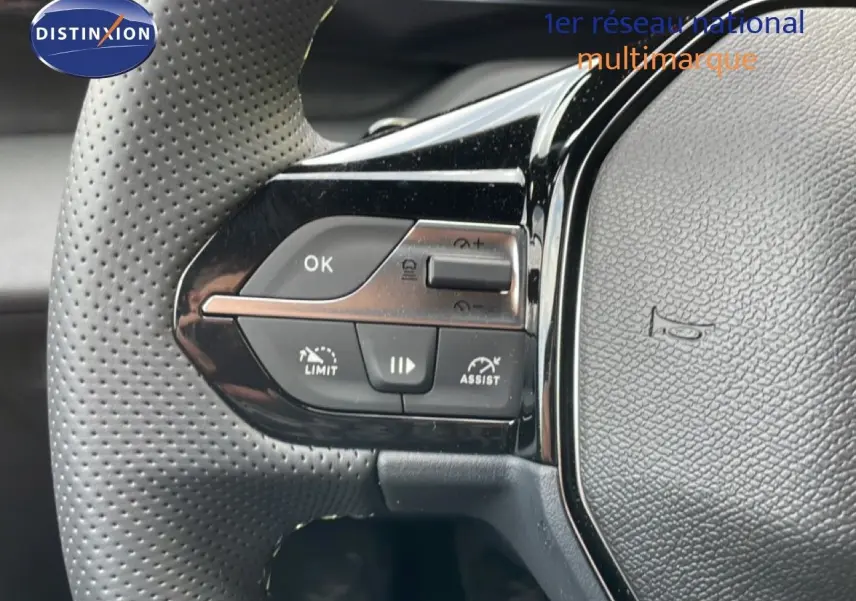 Gros plan sur les commandes gauche du volant perforé d'une Peugeot 308 gris Artense Hybrid 2026 avec boutons de limitation et assistance.