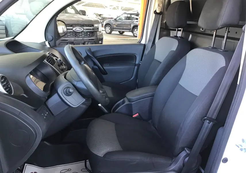 Vue intérieure côté conducteur du Renault Kangoo blanc 2021, montrant les sièges avant et le tableau de bord noir.