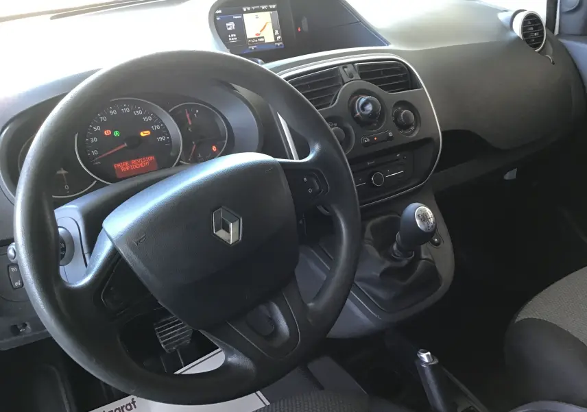 Vue intérieure du tableau de bord et volant noir d’un Renault Kangoo blanc 2021 avec levier de vitesses manuel et écran central.