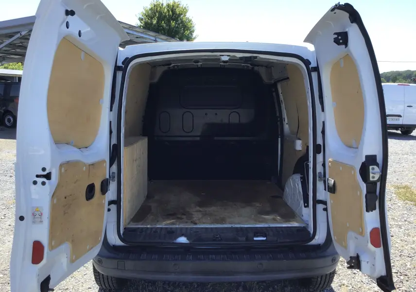 Vue arrière du Renault Kangoo blanc 2021 avec portes arrière ouvertes montrant l’espace de chargement vide et doublure bois.