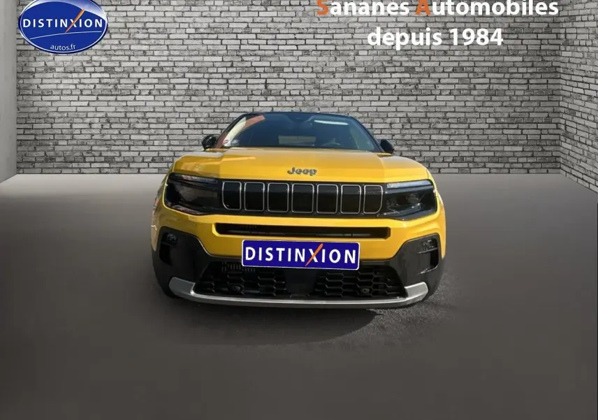 Vue frontale d'un Jeep Avenger jaune foncé avec calandre noire et logo Jeep visible sur fond de mur en briques.