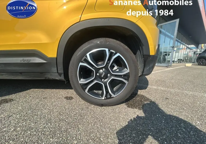 Gros plan sur la roue avant droite d’un Jeep Avenger jaune foncé avec logo Jeep sur le bas de caisse.
