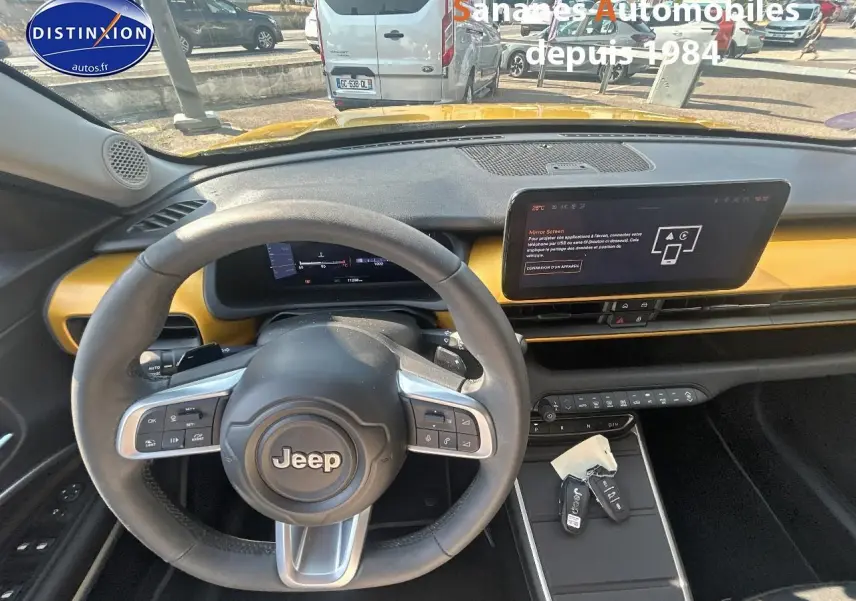 Vue intérieure du tableau de bord et volant Jeep Avenger jaune foncé, avec écran tactile et clés sur la console centrale.