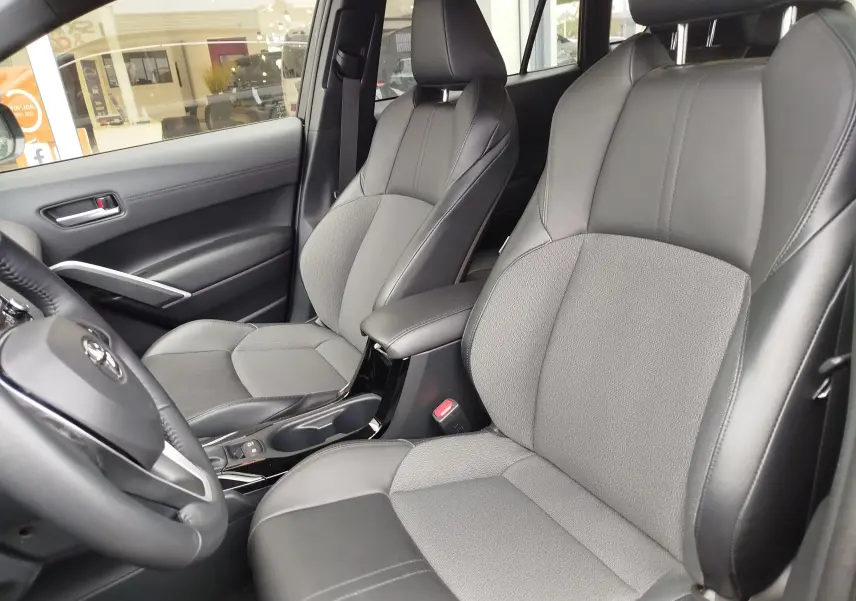 Vue intérieure côté conducteur montrant les sièges en tissu gris et cuir noir du Toyota Corolla Cross Hybrid 2025.