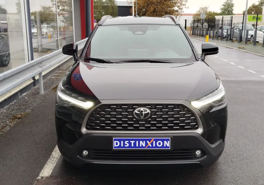 Vue avant d'une Toyota Corolla Cross Hybrid 140 Luxury Limited noire avec phares LED allumés sur un parking.