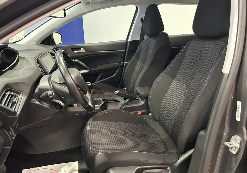 Vue intérieure côté conducteur de la Peugeot 308 gris 2021, sièges tissu noir à motif pied-de-poule et volant multifonction.