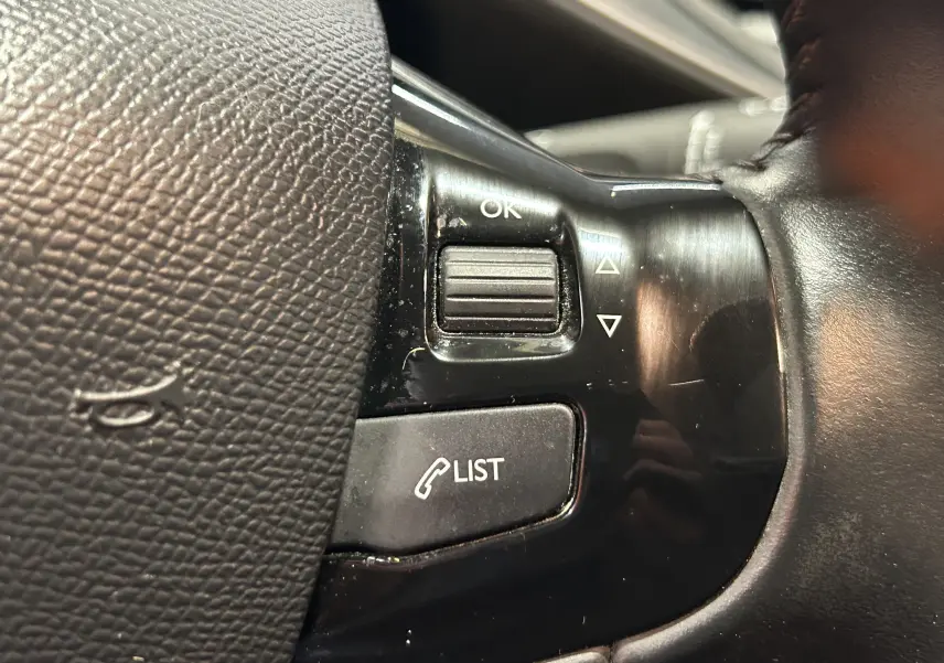 Gros plan sur les commandes au volant noir d'une Peugeot 308 Active Pack gris, avec bouton liste et molette OK.