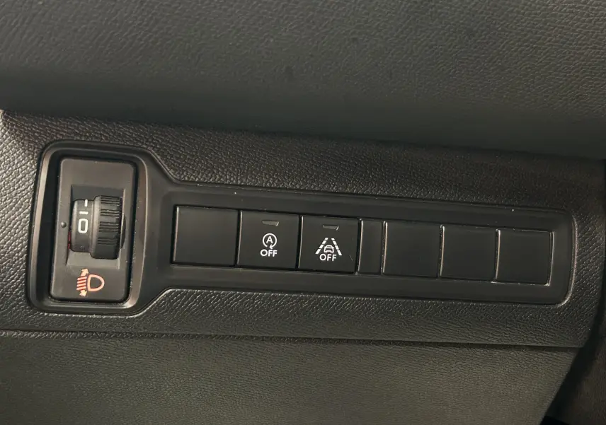 Gros plan sur les commandes noires du tableau de bord de la Peugeot 308 Active Pack gris, avec réglage phares et boutons d'assistance éteints.