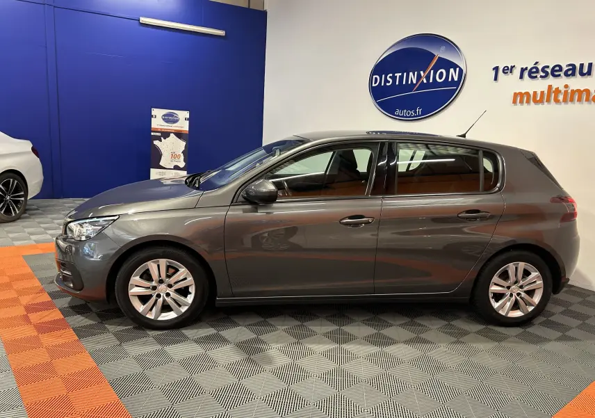 Profil côté gauche d'une Peugeot 308 Active Pack gris métallisé, compacte cinq portes en showroom lumineux.