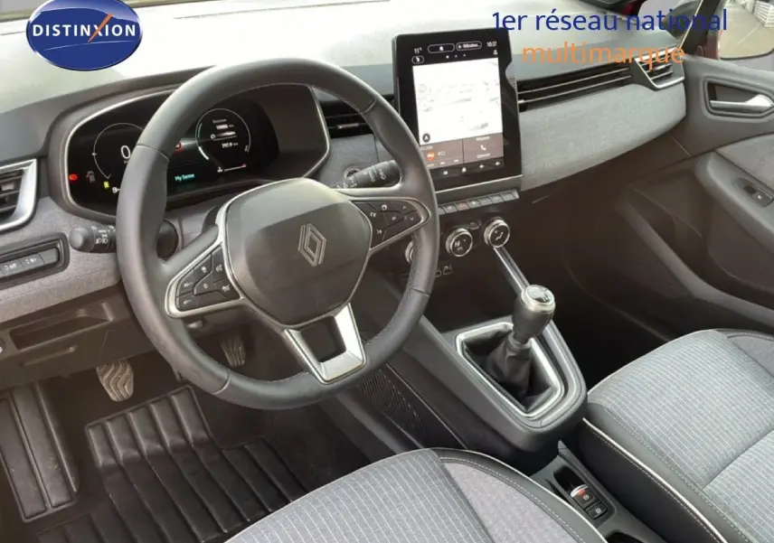 Vue intérieure de face du poste de conduite de la Renault Clio 2025, volant cuir, écran tactile et levier de vitesse manuel.