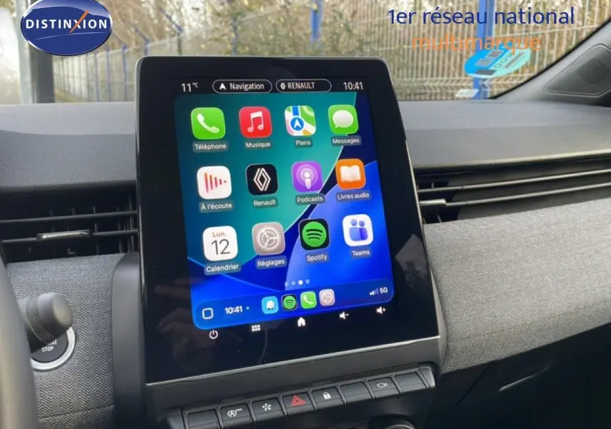 Intérieur de Renault Clio 2025, écran tactile central affichant applications, tableau de bord gris texturé visible.