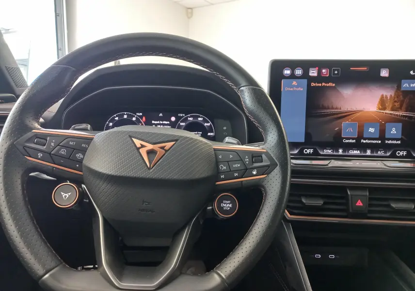 Vue intérieure centrée sur le volant noir perforé avec logo CUPRA cuivré et écran tactile du tableau de bord.