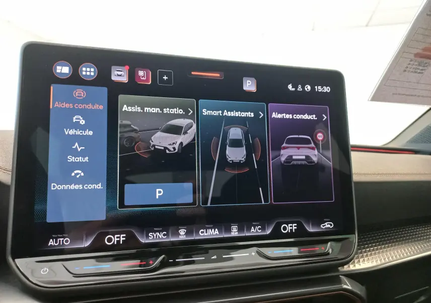 Écran tactile intérieur du CUPRA Leon Phase 2 montrant les aides à la conduite avec interface moderne et finition noire.