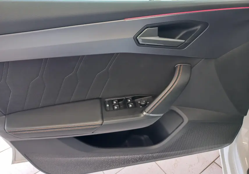 Intérieur côté gauche de la porte d’une CUPRA Leon blanc Nevada, avec garniture noire et surpiqûres orange.