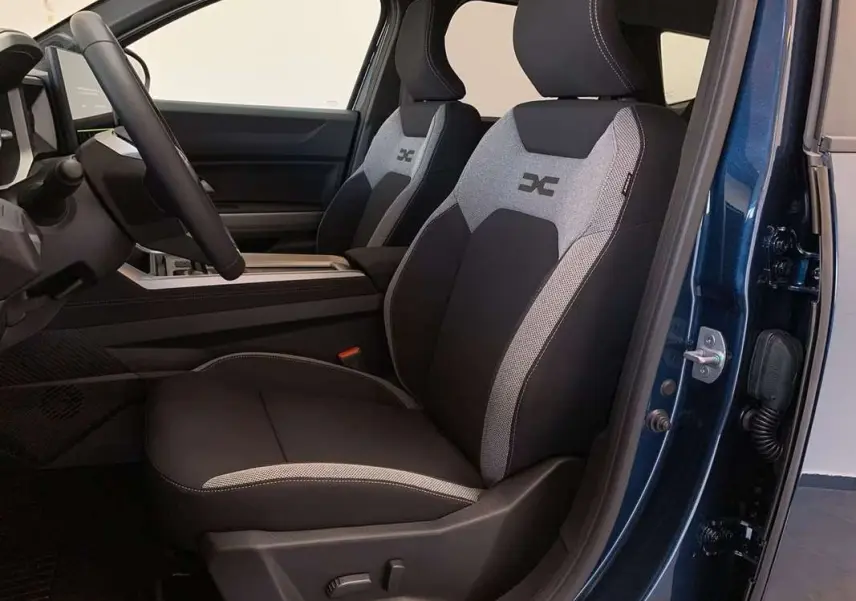 Vue intérieure côté conducteur du Dacia Bigster Hybrid 155 Journey Plus bleu indigo, sièges tissu noir et gris avec logo brodé.
