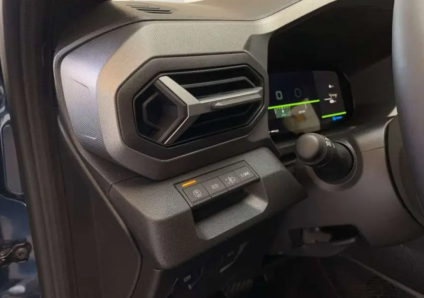Gros plan sur la console gauche du tableau de bord du Dacia Bigster bleu indigo, avec commandes et aérateur hexagonal.