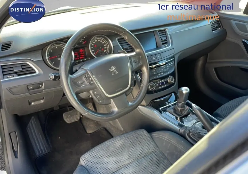 Vue intérieure côté conducteur du tableau de bord et volant noir d'une Peugeot 508 blanche de 2012 avec boîte automatique.