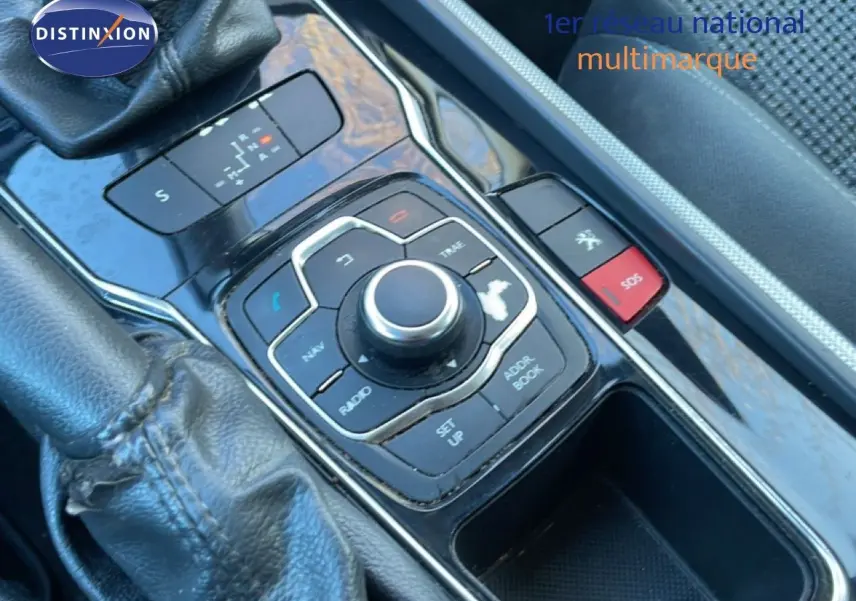 Gros plan sur la console centrale noire de la Peugeot 508 blanche, mettant en valeur la molette de commande multimédia et la commande de boîte auto.