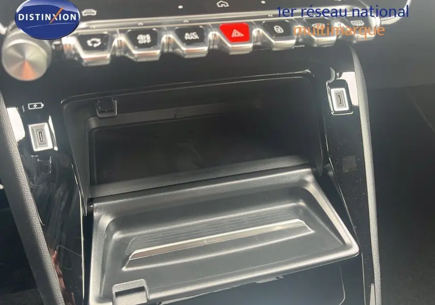 Gros plan sur la console centrale noire du Peugeot 2008 2025, montrant les boutons de commande et un rangement ouvert.