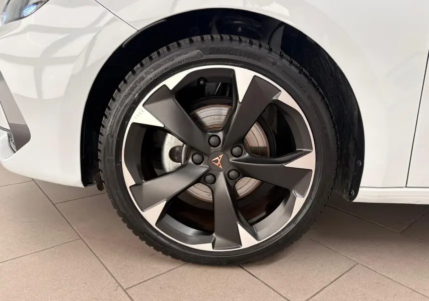 Gros plan sur la roue avant droite d'une CUPRA Leon blanc Nevada avec jante alliage sombre à cinq branches.