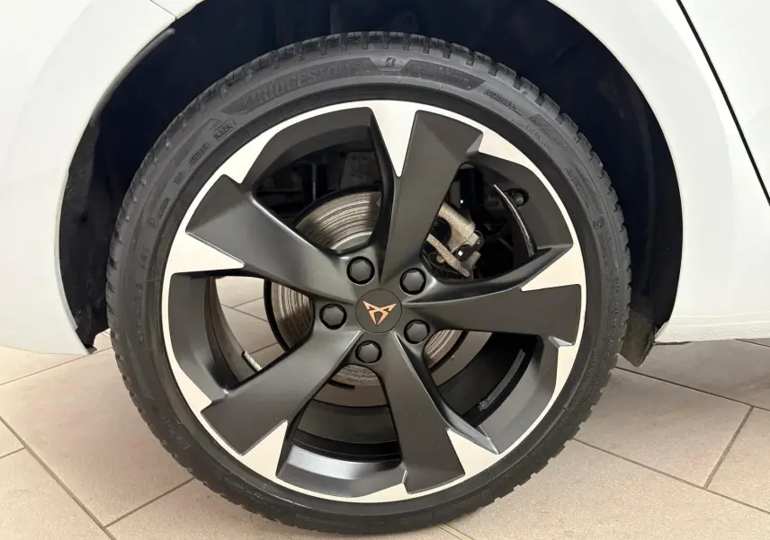 Gros plan sur la roue avant droite d'une CUPRA Leon blanc Nevada avec jante alliage noire et argentée au design distinctif.