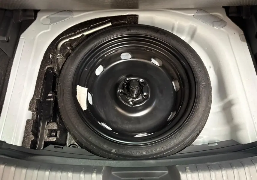 Gros plan sur la roue de secours noire dans le coffre blanc du CUPRA Leon Phase 2 2025.