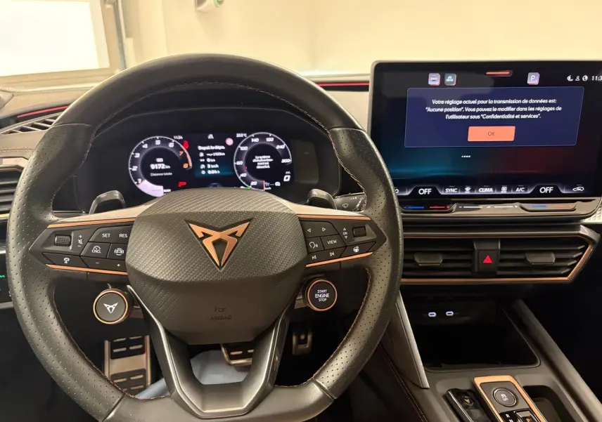 Vue intérieure centrée sur le volant CUPRA noir avec logo cuivré et tableau de bord numérique lumineux.