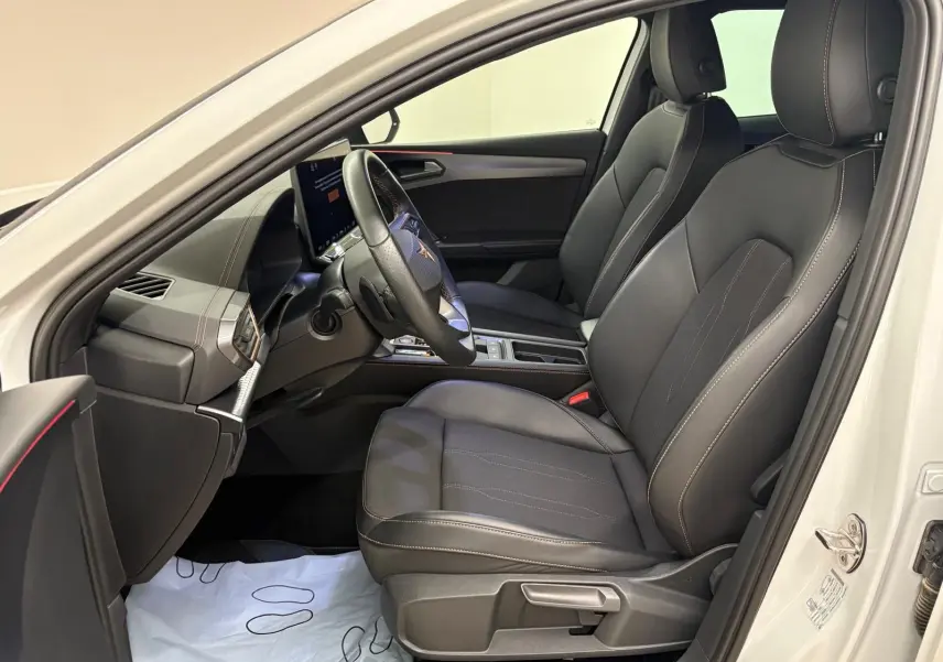 Vue intérieure côté conducteur de la CUPRA Leon blanc Nevada 2025, sièges noirs avec surpiqûres contrastantes et volant sport.