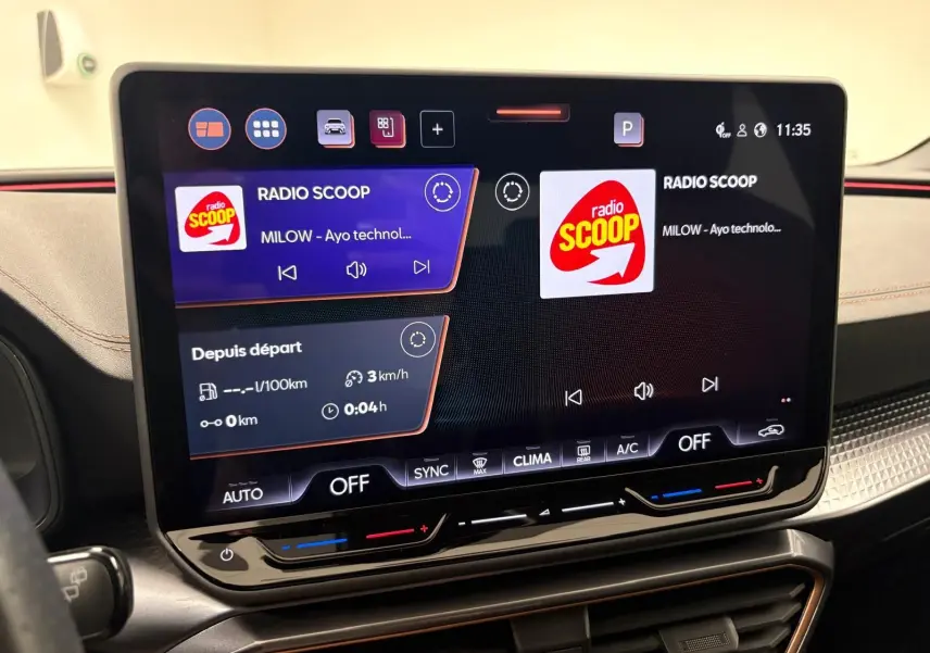 Écran tactile central du tableau de bord de la CUPRA Leon blanc Nevada, affichant la radio et les commandes climatiques.