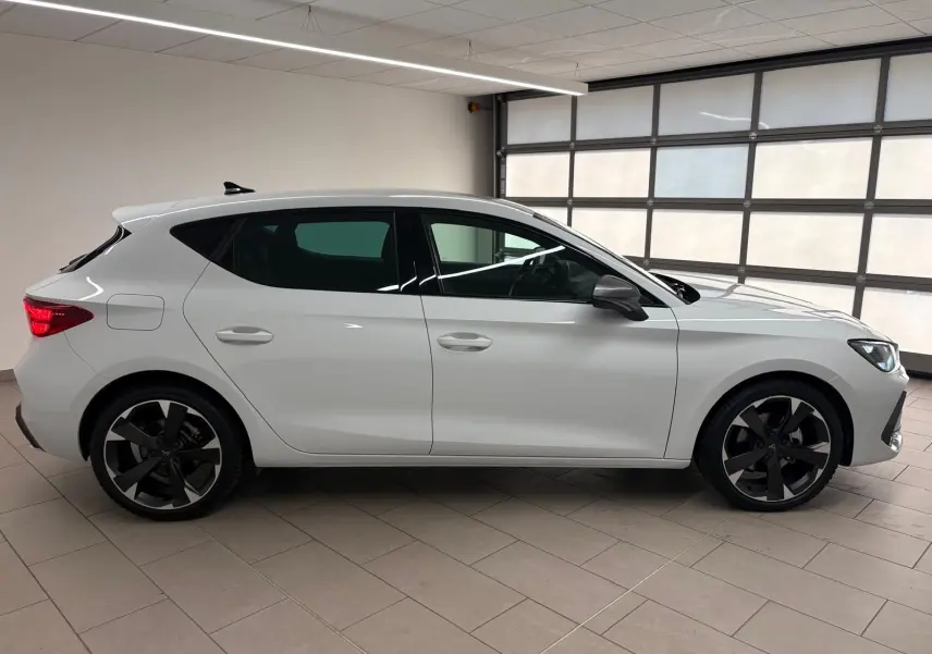 Vue de profil côté gauche d'une CUPRA Leon blanche Nevada 2025 avec jantes noires et vitres teintées.