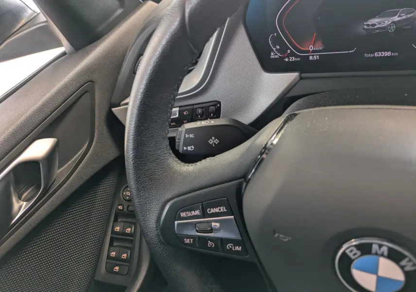 Vue rapprochée du volant et tableau de bord numérique d’une BMW Série 1 gris, avec commandes au volant visibles.