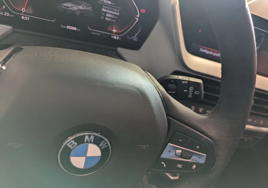 Vue rapprochée du volant cuir noir BMW Série 1 116d 2022 avec commandes intégrées et tableau de bord numérique.