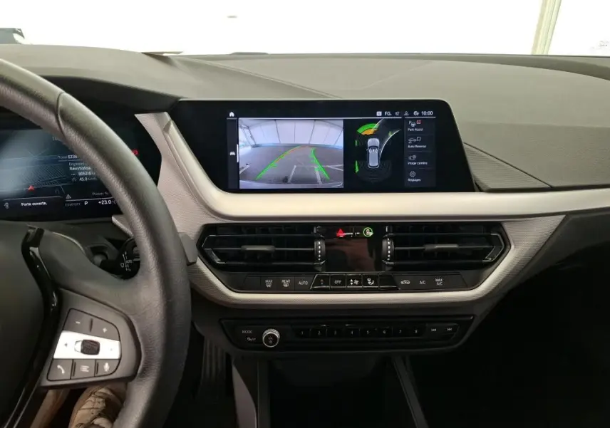 Coffre ouvert d’une BMW Série 1 gris montrant la roue de secours et les outils de bord rangés sous le plancher.