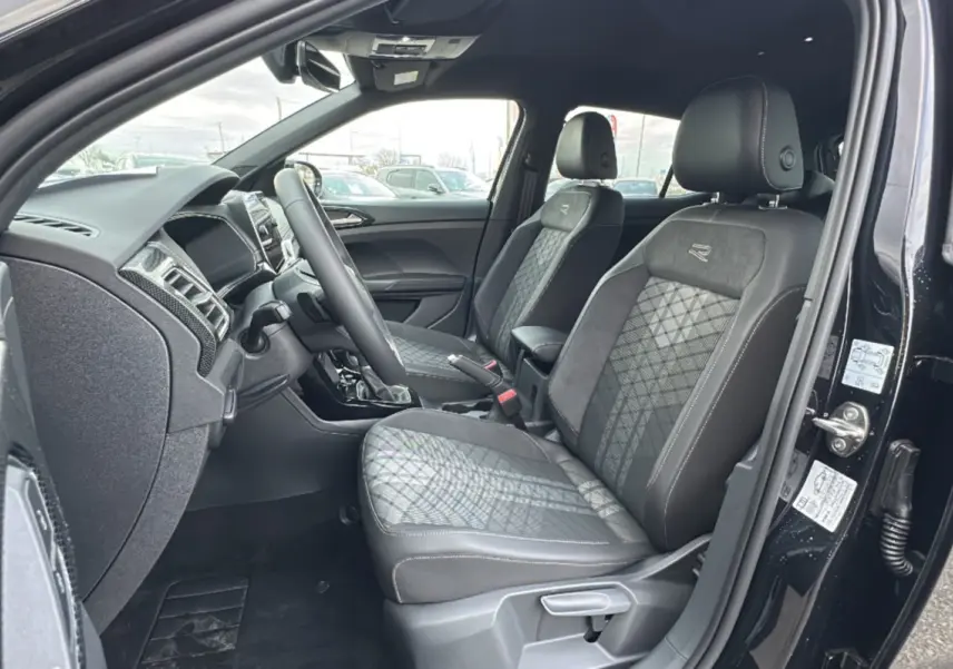 Vue intérieure côté conducteur du Volkswagen T-Cross noir intense 2025, sièges R-Line en tissu et alcantara avec surpiqûres contrastées.