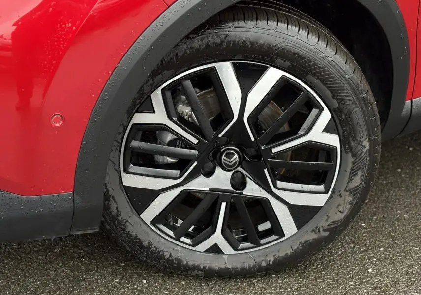 Gros plan sur la roue avant gauche de la Citroën C4 Hybrid 2025 en Rouge Elixir avec jante alliage 18 pouces diamantée.