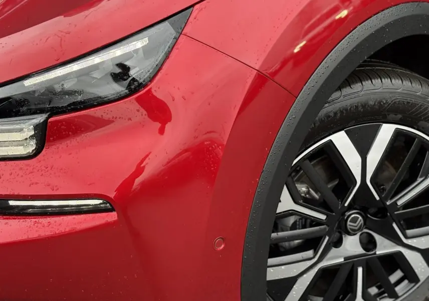 Gros plan sur l'avant droit rouge Elixir de la Citroën C4 Hybrid 2025 avec phares LED et jante alliage 18 pouces.