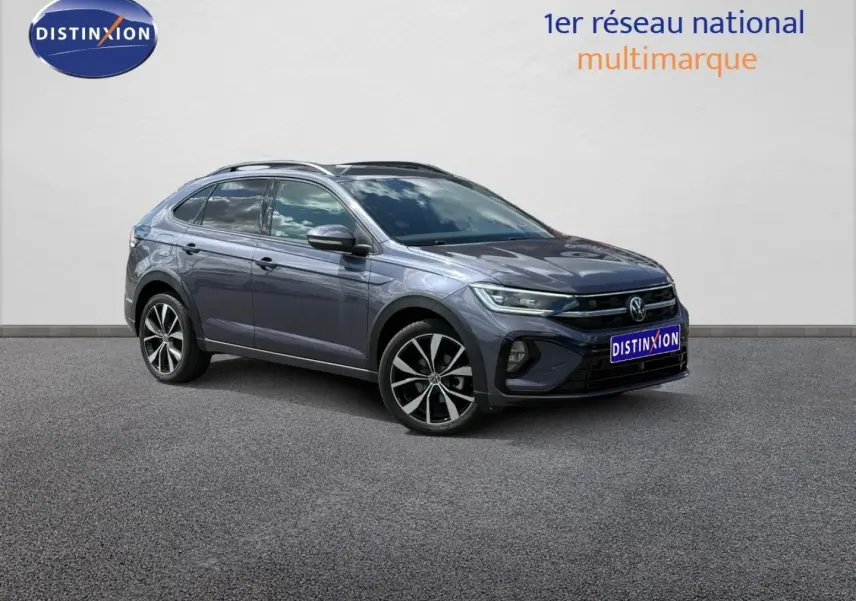 Volkswagen Taigo gris Ascot en 3/4 avant droit avec jantes alliage et barres de toit visibles.